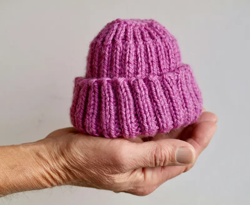 A small magenta ribbed knitted baby beanie held in an open palm