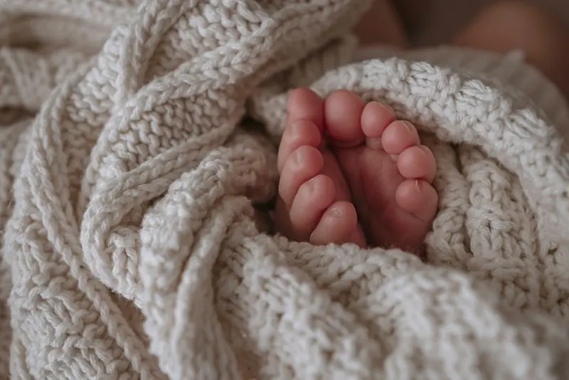 A baby's feet wrapped in a cream cable-knit blanket