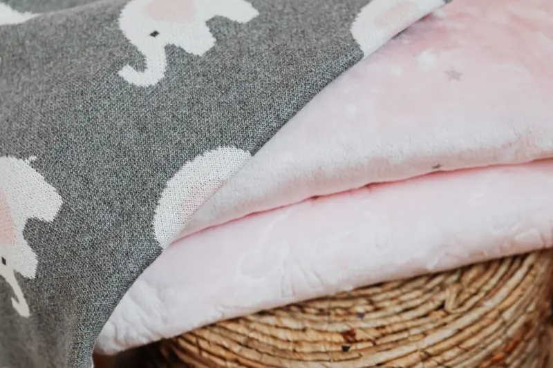 Folded grey and pink baby blankets resting on a woven basket