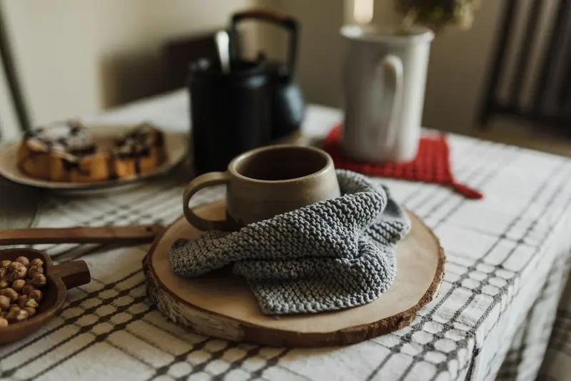 A light grey knitted cloth wrapped around a mug on a rustic wooden coaster