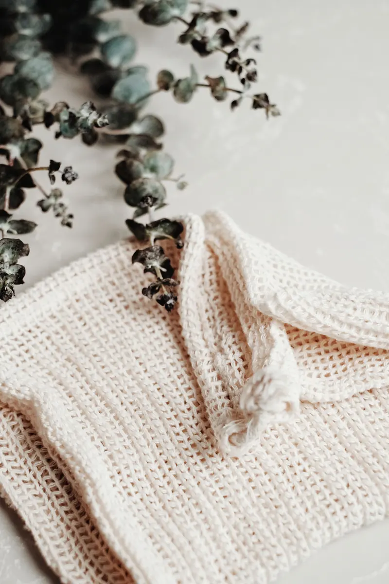 A cream knitted washcloth with a mesh texture beside dried eucalyptus