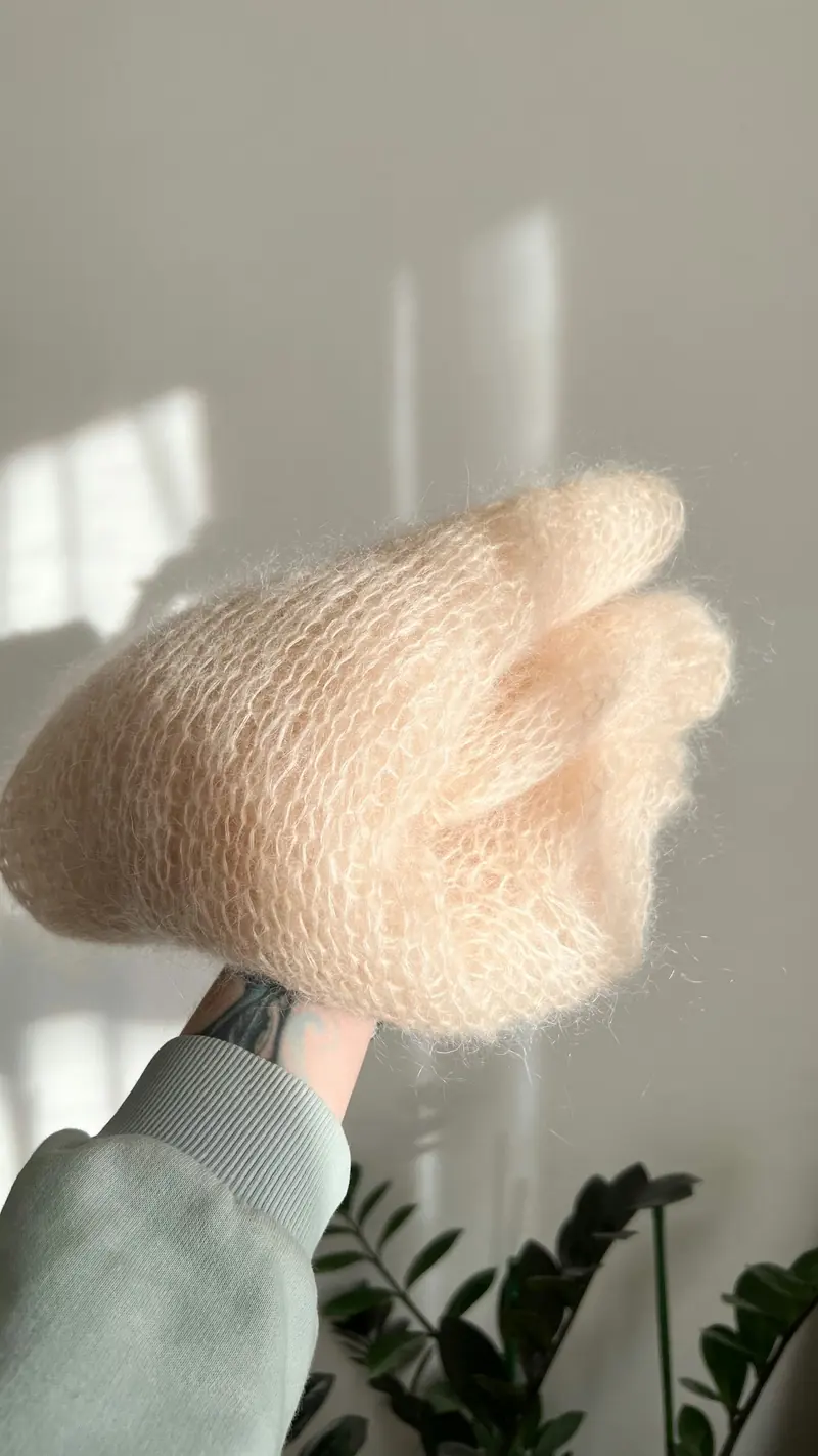 A hand holding a soft peach fuzzy knitted accessory in bright indoor light