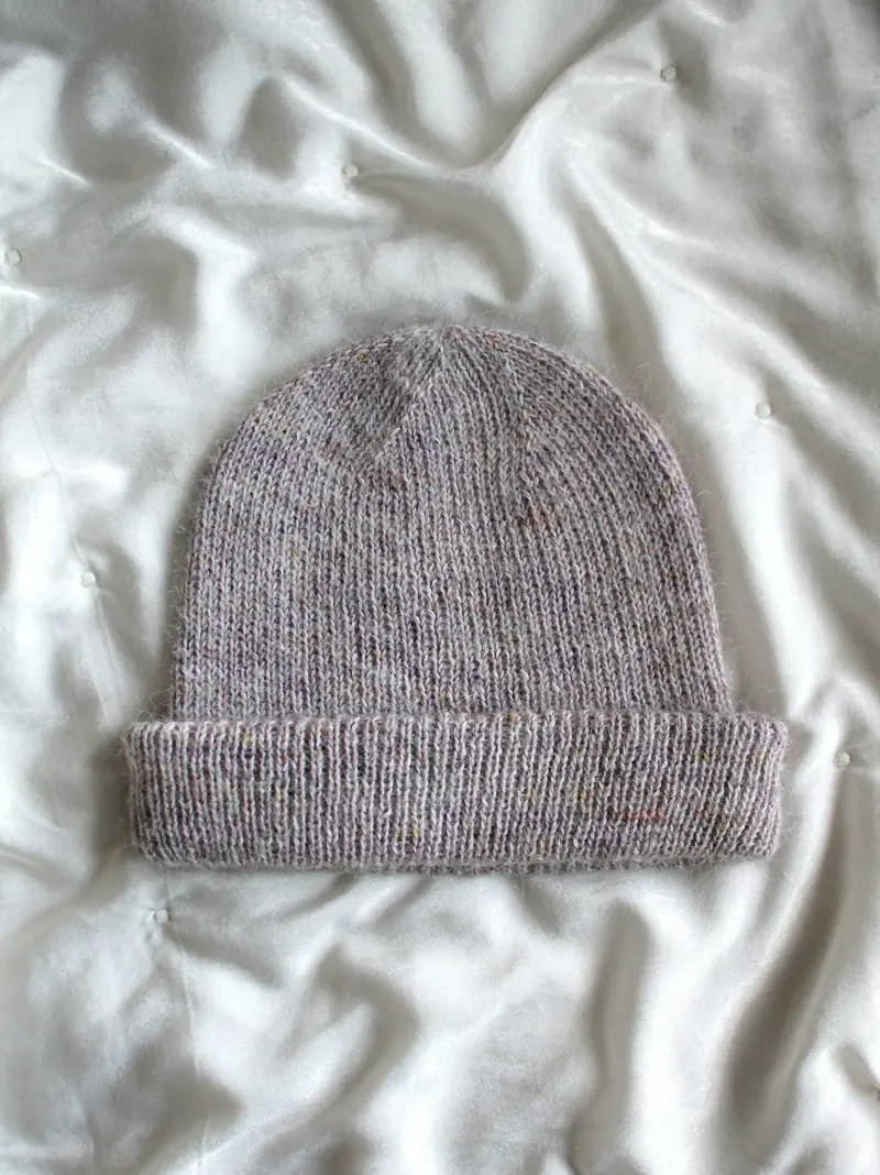 A dusty purple heathered knitted beanie with a ribbed brim on white quilted fabric