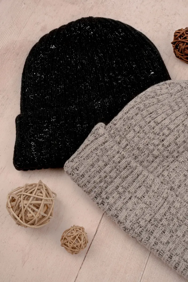 Two ribbed knitted beanies in black and heather grey on light wood with wicker balls