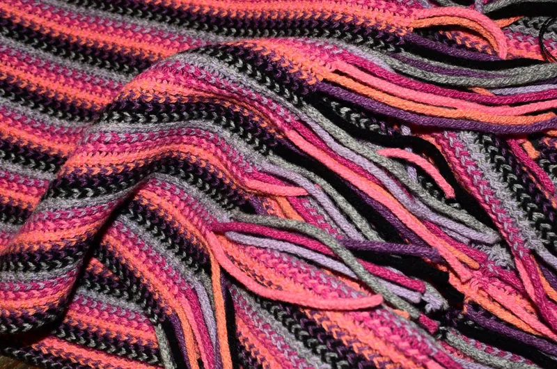 A bright pink, orange, grey, and black striped knitted scarf with fringe