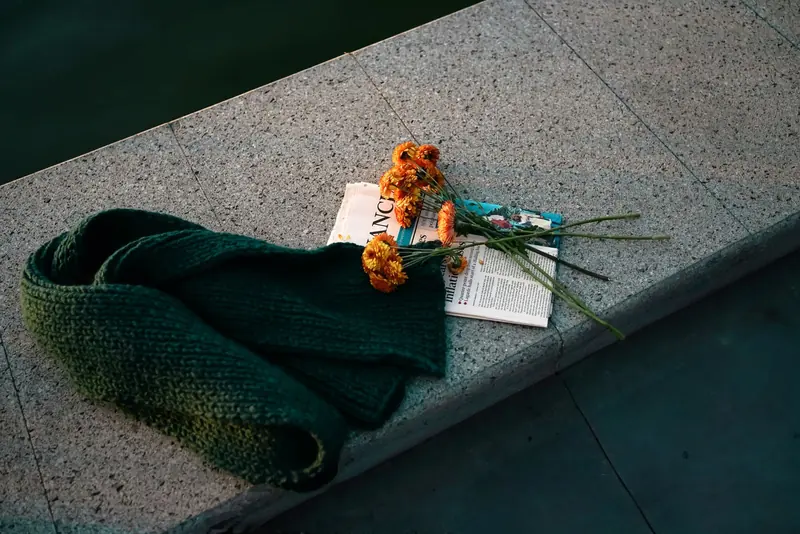 A chunky forest-green knitted scarf on a stone ledge beside orange flowers