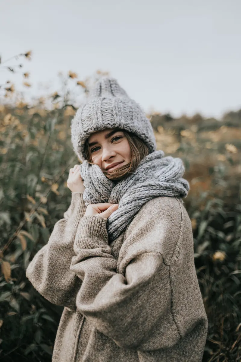 A person wearing a chunky grey knitted beanie and matching scarf in a field